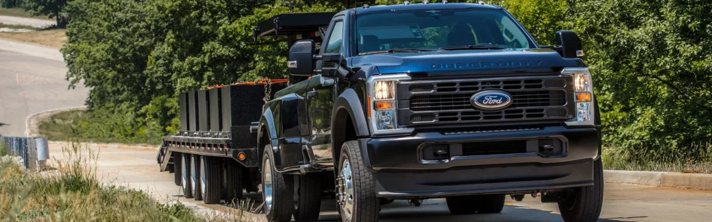 A black Ford Super Duty truck towing a large flatbed trailer down a rural road.